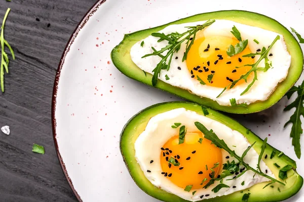 Fried eggs in avocado with fresh herbs and spices. Avocado stuffed with eggs. Delicious breakfast or snack on a light background, top view.