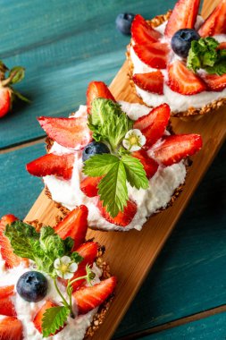 Kremalı, çilekli ve böğürtlenli meyveli turtalar ve tidewater yeşili arka plan. dikey görüntü. Kapat..