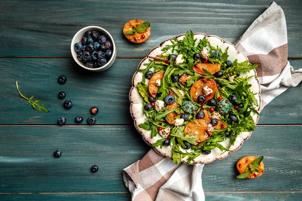 Easy recipe for summer salad with goat cheese, grilled apricots, arugula, berries, close-up on a plate wooden background, recipe top view.