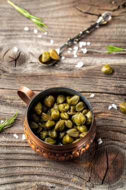 Ahşap arka planda kavanozda marine edilmiş kapari. dikey resim, metin için yer. Akdeniz, İtalyan, İspanyol, Fransız mutfağı için lezzetli malzemeler..