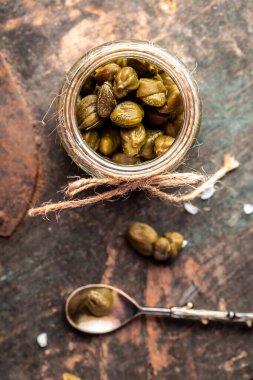 Kapari ahşap arka planda kavanozda marine edilmiş kapari. dikey resim, metin için yer. Akdeniz, İtalyan, İspanyol ve Fransız mutfağı için lezzetli malzemeler. Turşu turşusu. Konserve kapari..