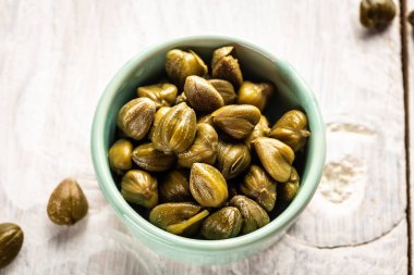 Seramik kasede marine edilmiş kapari. Capparis spinosa 'nın yenilebilir çiçek tomurcukları, kapari çalıları ya da Çakmaktaşlar hafif arka planda yükseldi.