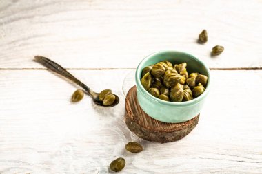 Seramik kasede marine edilmiş kapari. Capparis spinosa 'nın yenilebilir çiçek tomurcukları, kapari çalıları ya da Çakmaktaşlar hafif arka planda yükseldi.