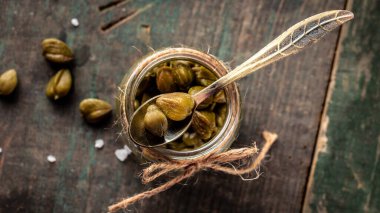 Koyu ahşap arka planda turşulu kapari. CapParis 'in yenilebilir çiçek tomurcukları, kapari çalıları ya da Çakmaktaşlar gülü. Yemek yapmak için lezzetli malzemeler..