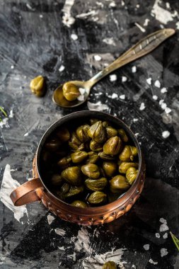 Koyu arkaplandaki kapari kavanozunda marine edildi. Akdeniz, İtalyan, İspanyol ve Fransız mutfağı için lezzetli malzemeler. Turşulu, konserve kapari. dikey resim.