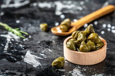 Woden kasesinde marine edilmiş kapari. Capparis spinosa 'nın yenilebilir çiçek tomurcukları, gebre çalıları veya Çakmaktaşlar koyu bir arka planda yükseldi..