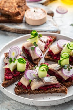 Ringa balıklı sandviç, pancar, yeşil salatalık, soğan ve mikroyeşil. Siyah ekmek tostu. Geleneksel Danimarka İskandinav mutfağı. dikey resim, üst görünüm.