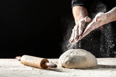Un ve un serpintili erkek eli fotoğrafı. Ekmek pişiriyorum. Hamuru yoğurmak. Karanlık arka planda izole edilmiş. Metin için boş boşluk.