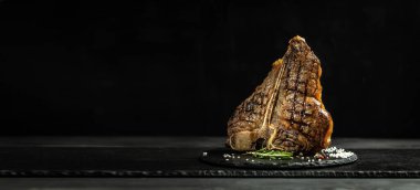 Bir parça pişmiş T-bone ya da yıllanmış wagyu bifteği ızgara biftek ve taş tahtada servis edilmiş baharatlar. Uzun pankart biçimi, üst görünüm.