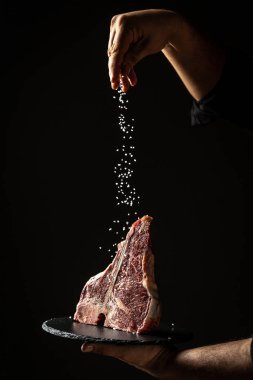 Şefin elleri, kurutulmuş wagyu bifteği büyük parça fileto ile pişiriyor. Siyah arka planda dondurucu hareketle tuz ve biber ekliyor. dikey resim, metin için yer.