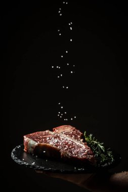 Şefin elleri, kurutulmuş wagyu bifteği büyük parça fileto ile pişiriyor. Siyah arka planda dondurucu hareketle tuz ve biber ekliyor. dikey resim, metin için yer.
