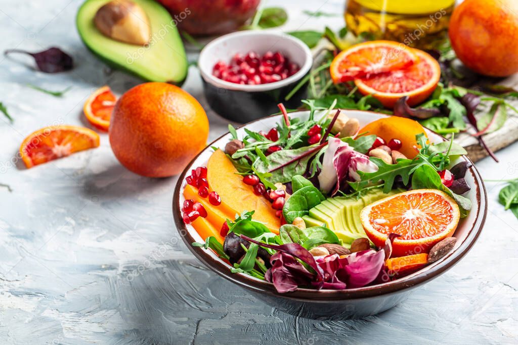 Healthy vegetable buddha bowl lunch with avocado, persimmon, blood orange, nuts, spinach, arugula and pomegranate on a light background, top view