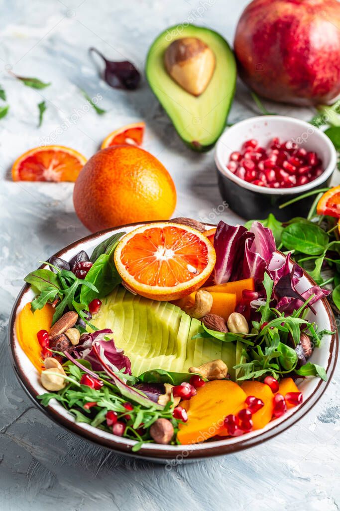 Buddha bowl of mixed vegetables and friit with avocado, persimmon, blood orange, nuts, spinach, arugula and pomegranate. Healthy balanced eating. Top view. vertical image.