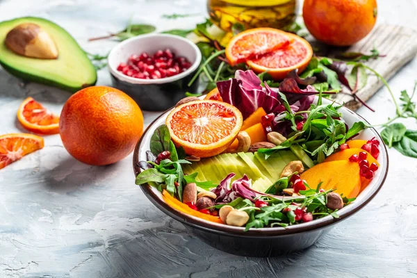 Buddha bowl dish with avocado, persimmon, blood orange, nuts, spinach, arugula and pomegranate. Healthy balanced eating. Top view.