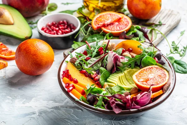 Buddha bowl, healthy and balanced food avocado, persimmon, blood orange, nuts, spinach, arugula and pomegranate. Healthy balanced eating. Top view.