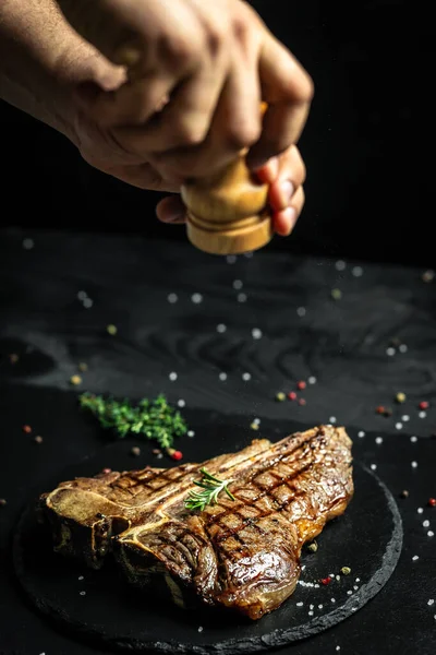 Grilled Porterhouse steak. Chef season salt on a juicy beef steak in a restaurant. in a freeze motion. American meat restaurant. banner, catering menu recipe place for text.