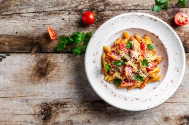 Çeri domates soslu makarna makarna, tavuk eti ve rendelenmiş parmesan peyniri. Kırsal ahşap masada Pomodoro makarnası. İtalyan yemeği. Üst görünüm.