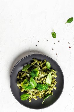 Yeşil brokoli makarna ve taze ıspanak yaprakları açık arkaplanda siyah bir kâsede. dikey resim, metin için yer. en üstteki görünüm.