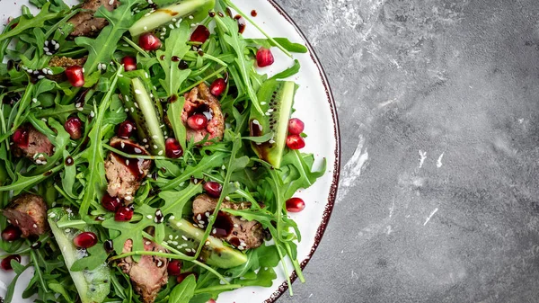 Diet menu. Healthy salad of fresh arugula, chicken liver, kiwi and pomegranate on a bowl. Flat lay. Banner. Top view.