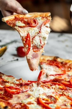 Biberli bir dilim pizza, domates, arka planda jambon. İtalyan mutfağı. Yemek tarifi geçmişi. Kapat..