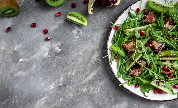 Diet menu. Healthy salad of fresh arugula, chicken liver, kiwi and pomegranate on a bowl. Flat lay. Banner. Top view.