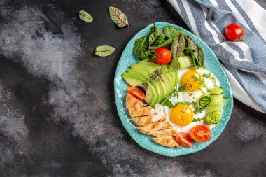 Keto diyet yemekli tabak. Kızarmış yumurta, kiraz domatesleri, avokado, tavuk ızgara fileto, salatalık ve avokado. Sağlıklı kahvaltı. en üstteki görünüm.