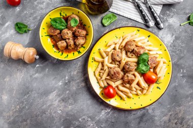 Köfteli makarna ve sarı tabakta domates sosu ve gri arka planda İtalyan makarnası..