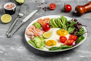 Ketojenik kahvaltı. Keto düşük karbonhidratlı somon, haşlanmış karides, karides, kızarmış yumurta, taze salata, domates, salatalık ve avokado. Üst görünüm.