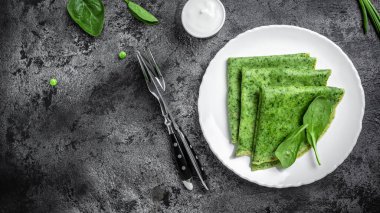 Koyu arkaplanda ıspanak yeşili krep. Beyaz tabakta nefis sağlıklı kahvaltı. afiş, metin için menü tarifi yeri, üst görünüm.