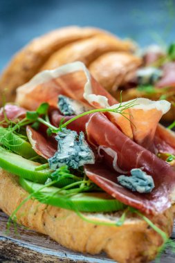Prosciutto, jamon, mavi peynir, avokado ve mikrocinle birlikte açık sandviç kruvasanı. Akdeniz aperatifi. Kahvaltı konsepti, yemek tarifi geçmişi. dikey resim,