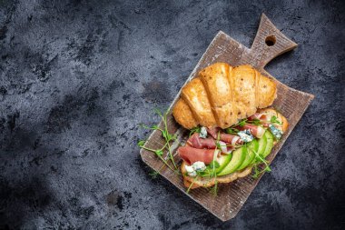 Close up Croissant sandwich with jamon serrano, prosciutto ham , blue cheese, avocado, microgin. mediterranean snacks. banner, menu recipe place for text, top view. clipart