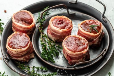 Çiğ mermer et, biftek fileminyonu. Et tepsisinde servis edilen domuz pastırmasına sarılı sığır filetosu bifteği. en üstteki görünüm.