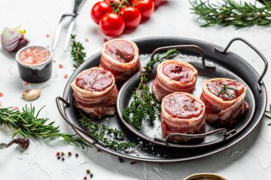 Domuz pastırmasına sarılı çiğ domuz eti bifteği hafif arka planda baharat, tuz ve biberli et tepsisinde servis edilir. Uzun pankart biçimi, üst görünüm.