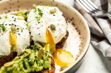 Avokado tostu ve arka planda haşlanmış yumurta, üst manzara. Vejetaryen yemeklerle kahvaltı, sağlıklı beslenme konsepti. Yemek tarifi geçmişi. Kapat..