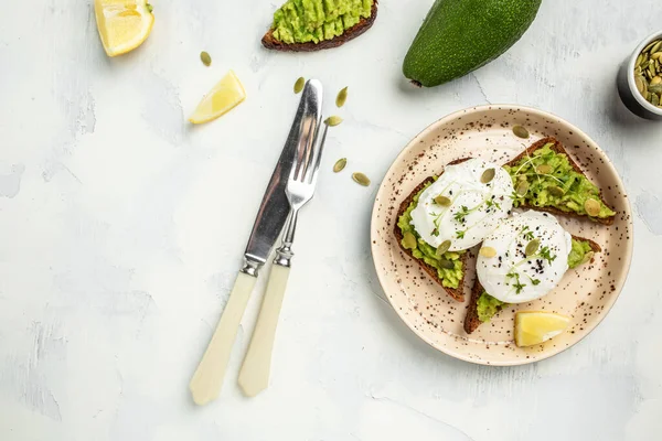 Avocado Sandwich with Poached Egg and avocado on toasted bread. Delicious breakfast or snack on a light background, top view.