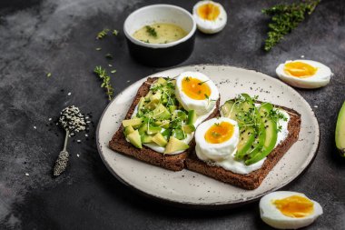 Haşlanmış yumurtalı avokado sandviçi ve mısır gevreği ekmeğinde yumuşak peynir. Siyah arkaplan, üst görünüm.