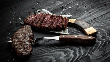 Geleneksel Amerikan barbeküsü bir tahta kasap ve çatalla dilimlenmiş kuru biftek. afiş, metin için menü tarifi yeri, üst görünüm.