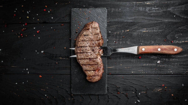 Rump Steak on fork on dark wooden background. banner, menu recipe place for text, top view.