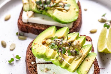 Kahvaltıda sağlıklı avokado tostları ya da öğle yemeğinde çavdar ekmeği, dilimlenmiş avokado, peynir, balkabağı ve susam tohumları. Pankart, yemek tarifi üst görünümü.