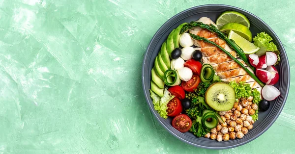 Buddha bowl dish with chicken fillet, avocado, asparagus, chickpeas, broccoli, radish, chicken, cucumber tomatoes olives mozzarella. Healthy balanced eating. Top view.