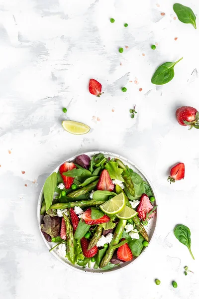 Diet menu. Healthy salad of fresh green asparagus, strawberry, rocket and cottage cheese. vertical image, place for text. Top view.