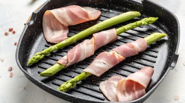 Izgara tavada domuz pastırmasına sarılmış yeşil kuşkonmaz, yemek tarifi geçmişi. Kapat.,