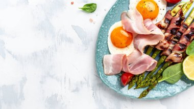 Kahvaltıda. Kızarmış yumurta, pastırmaya sarılmış kuşkonmaz, jambon, domates ve salata. Ketogenik, keto yemeği. Uzun pankart biçimi, üst görünüm.