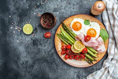 Lezzetli bir kahvaltı. Yeşil kuşkonmaz, pastırma, jambon ve vişneli domatesli yumurta. Sağlıklı dengeli yiyecekler. Üst görünüm, yukarıda, afiş.