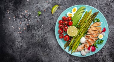 kuşkonmaz, tavuk fileto, vişneli domates, avokado, bıldırcın yumurtası ve turp siyah masada servis edilir. Keto kahvaltısı. afiş, metin için menü tarifi yeri, üst görünüm.