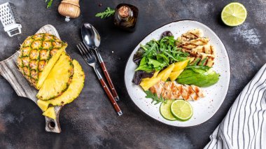 Sağlıklı bir akşam yemeği. Izgara tavuk göğsü, halloumi, ananas, avokado, yeşil roket salatası, limon ve zeytinyağı. gri arka planda. Düz yatıyordu. Üst görünüm,