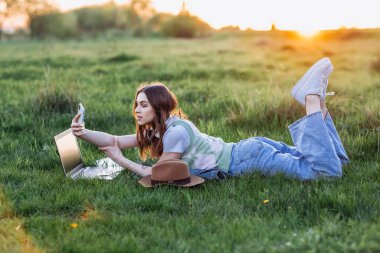 Laptop bilgisayar ve cep telefonu kullanan kulaklıklı genç bayan. Gün batımı ışığı. Yaşam tarzı kavramı.
