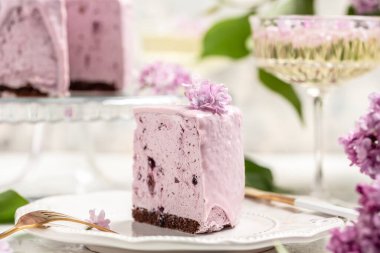 Bir parça kremalı pasta, taze böğürtlenli lezzetli tatlı yaban mersini turtası ve bir buket mor çiçek açan leylak, metin için dikey imge yeri.,