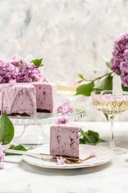 Bir parça kremalı pasta, taze böğürtlenli lezzetli tatlı yaban mersini turtası ve bir buket mor çiçek açan leylak, metin için dikey imge yeri.,