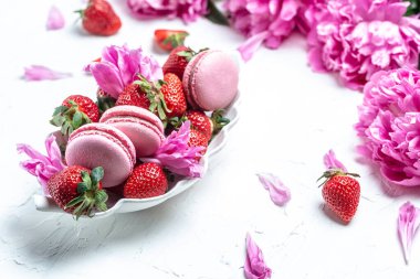 Pink peony rose flower and macaroni cookies and sweet strawberry on a white background. Small French cakes Macarons with fruit. top view.